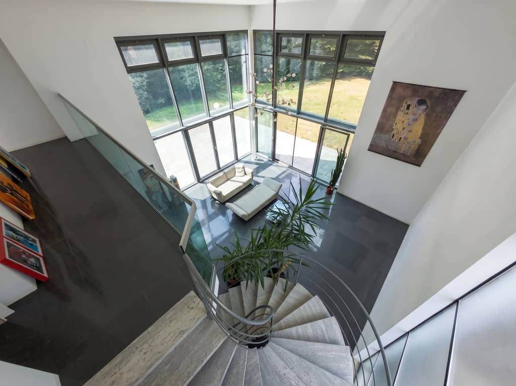Blick über die gewendelte Treppe und das Glasgeländer in den Luftraum des Wohnbereichs